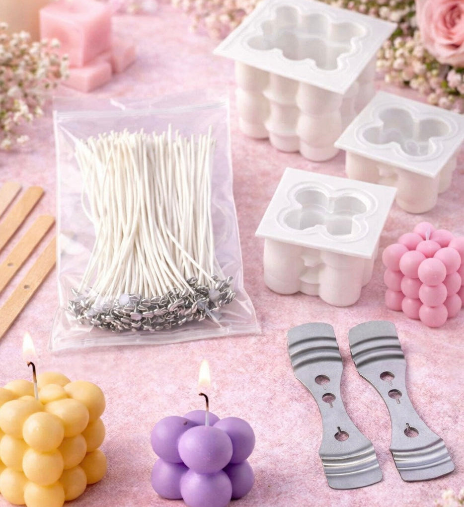 Candle-making supplies including molds, wicks, and candles on a pink surface with flowers.