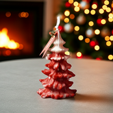 Red Christmas tree-shaped candle on a table with a fireplace and decorated tree in the background