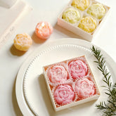Decorative boxes with pink rose-shaped candies on a white plate with a candle in the background.
