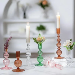 Set of colorful glass candle holders and vases on a white surface with a blurred indoor background.