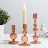 Set of three glass candle holders with a lit candle on a white surface.