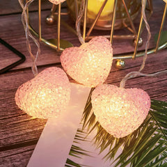 Heart-shaped string lights on a wooden surface with leaves in the foreground
