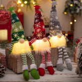 Three illuminated Christmas gnomes with colorful hats on a wooden surface.