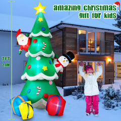 Inflatable Christmas tree with decorations and a child in front, set against a snowy house exterior.