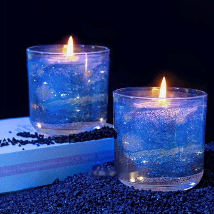 Two lit candles in glass containers with blue glitter on a dark background