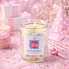 Candle in a glass jar labeled 'Happy Birthday' with a festive background including a party hat and pink decorations.