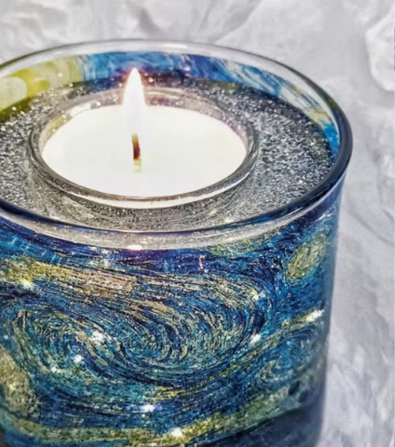 Candle in a glass holder with a swirling blue and gold design on a white background