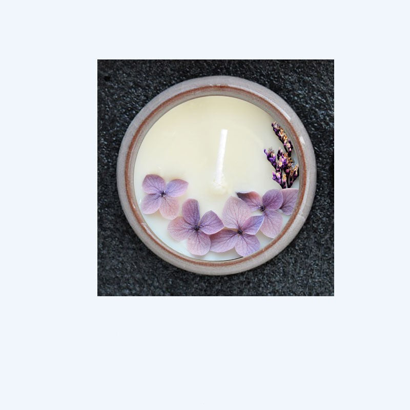 Candle with purple flowers in a white container on a dark surface