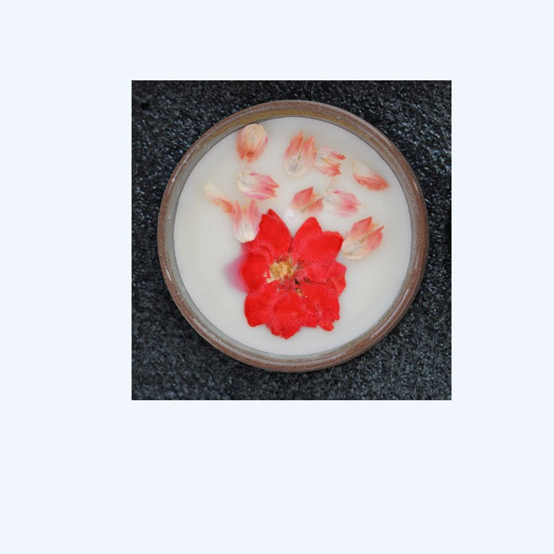 Candle with red flower in a circular container on a textured surface