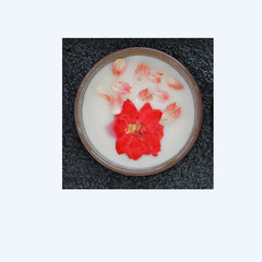 Candle with red flower in a circular container on a textured surface