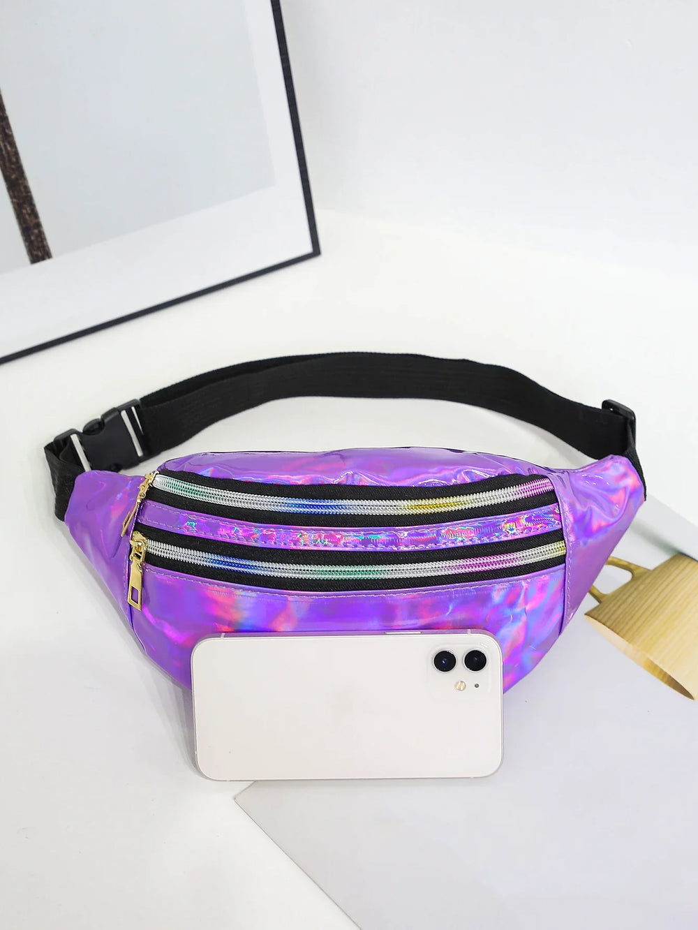 Holographic fanny pack on a white surface with a phone and laptop.