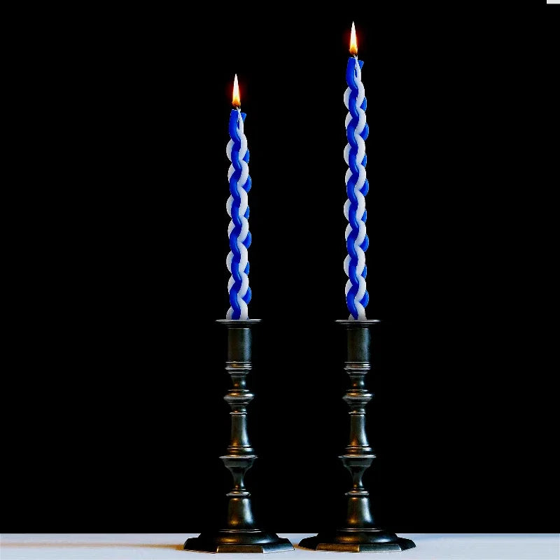Two blue twisted candles in black candlesticks against a black background