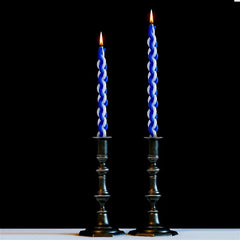 Two blue twisted candles in black candlesticks against a black background