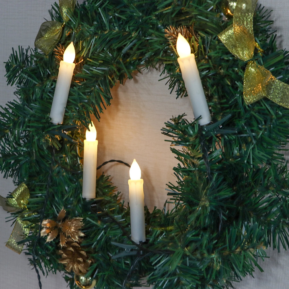 Decorative wreath with lit candles and gold bows on a plain background