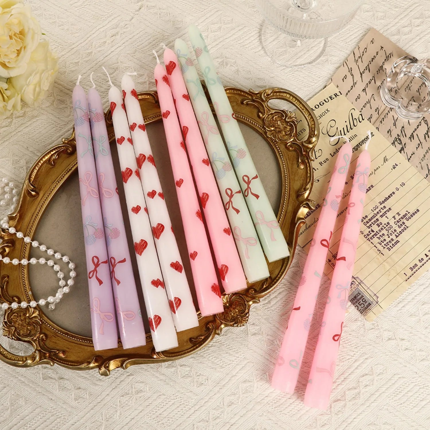 Decorative candles with heart and bow patterns on a textured surface with a vintage frame and paper.