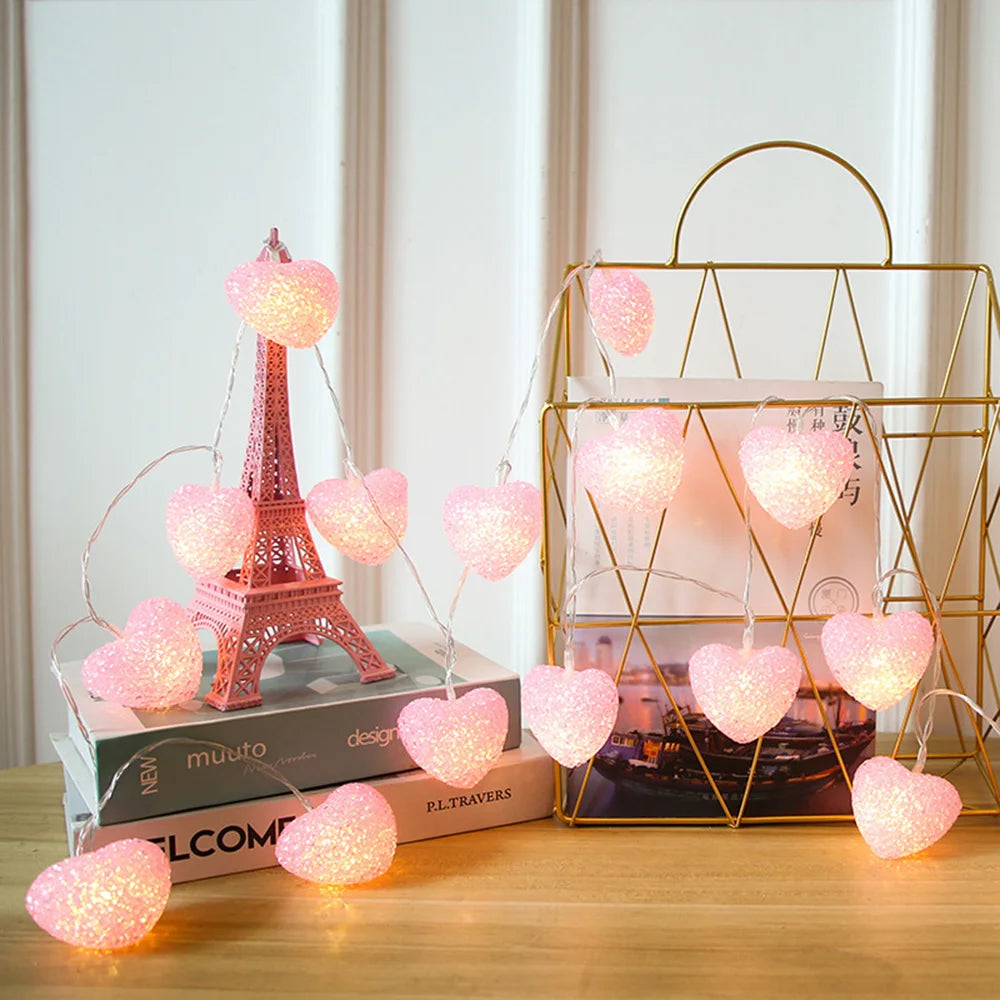 Decorative string lights shaped like hearts with a miniature Eiffel Tower and books on a wooden surface.