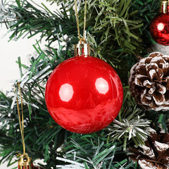 Red Christmas ball ornament hanging on a tree with pine cones and other decorations.