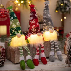 Three illuminated Christmas gnomes with colorful hats on a wooden surface.