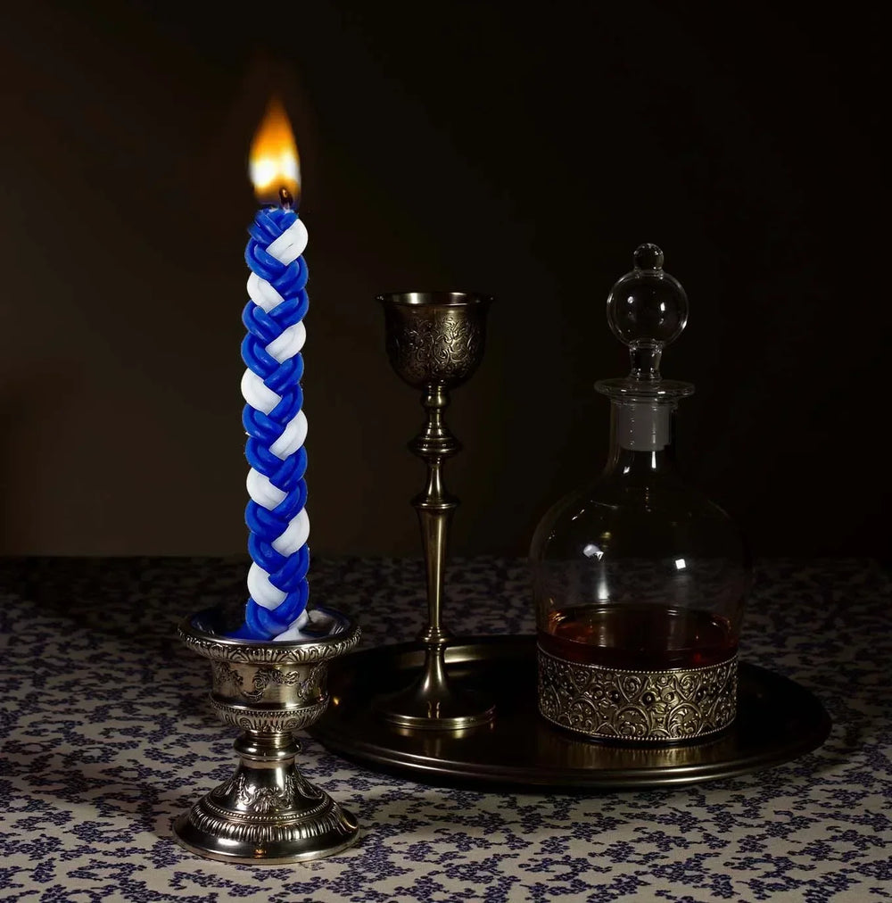 Blue and white braided candle with a silver holder on a dark background