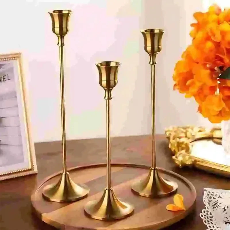 Three gold candle holders on a wooden tray with a decorative background