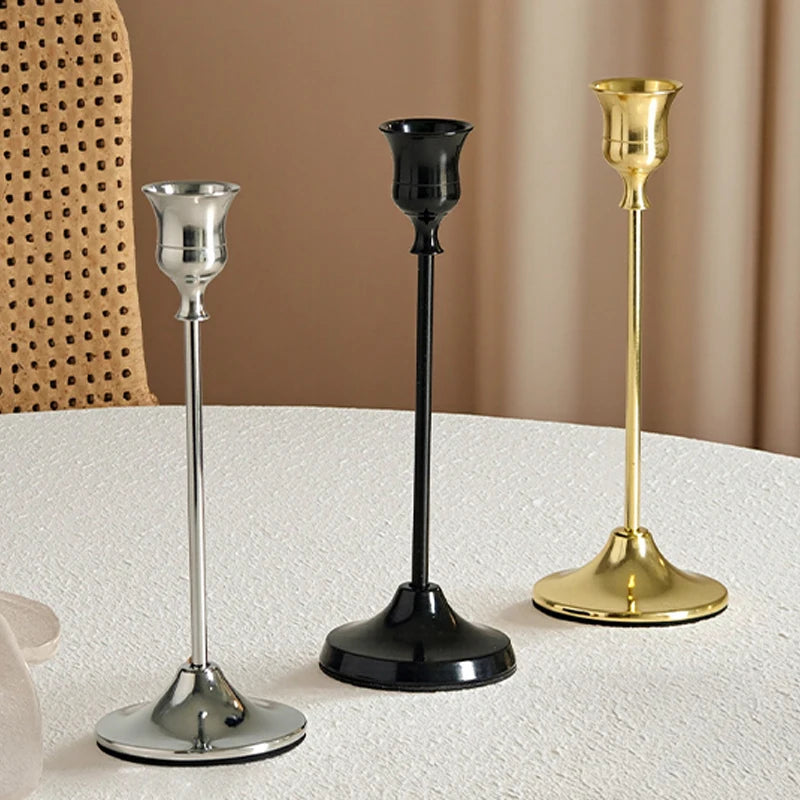 Three metallic candle holders in silver, black, and gold on a textured surface.