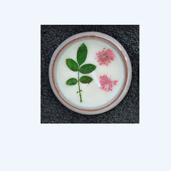 Round white object with green leaves and pink flowers on a dark textured background