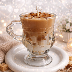 Glass mug with layered coffee drink on a white marble coaster, surrounded by cinnamon sticks and sugar cubes.