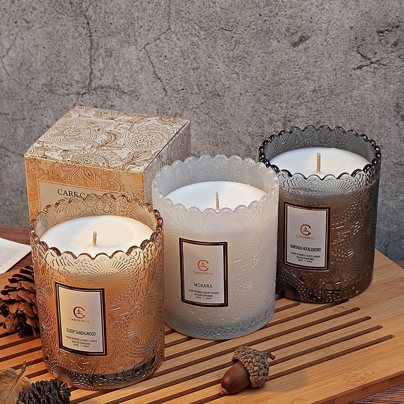 Three candles with decorative containers on a wooden surface with a textured gray wall background.