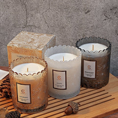 Three candles with decorative containers on a wooden surface with a textured gray wall background.