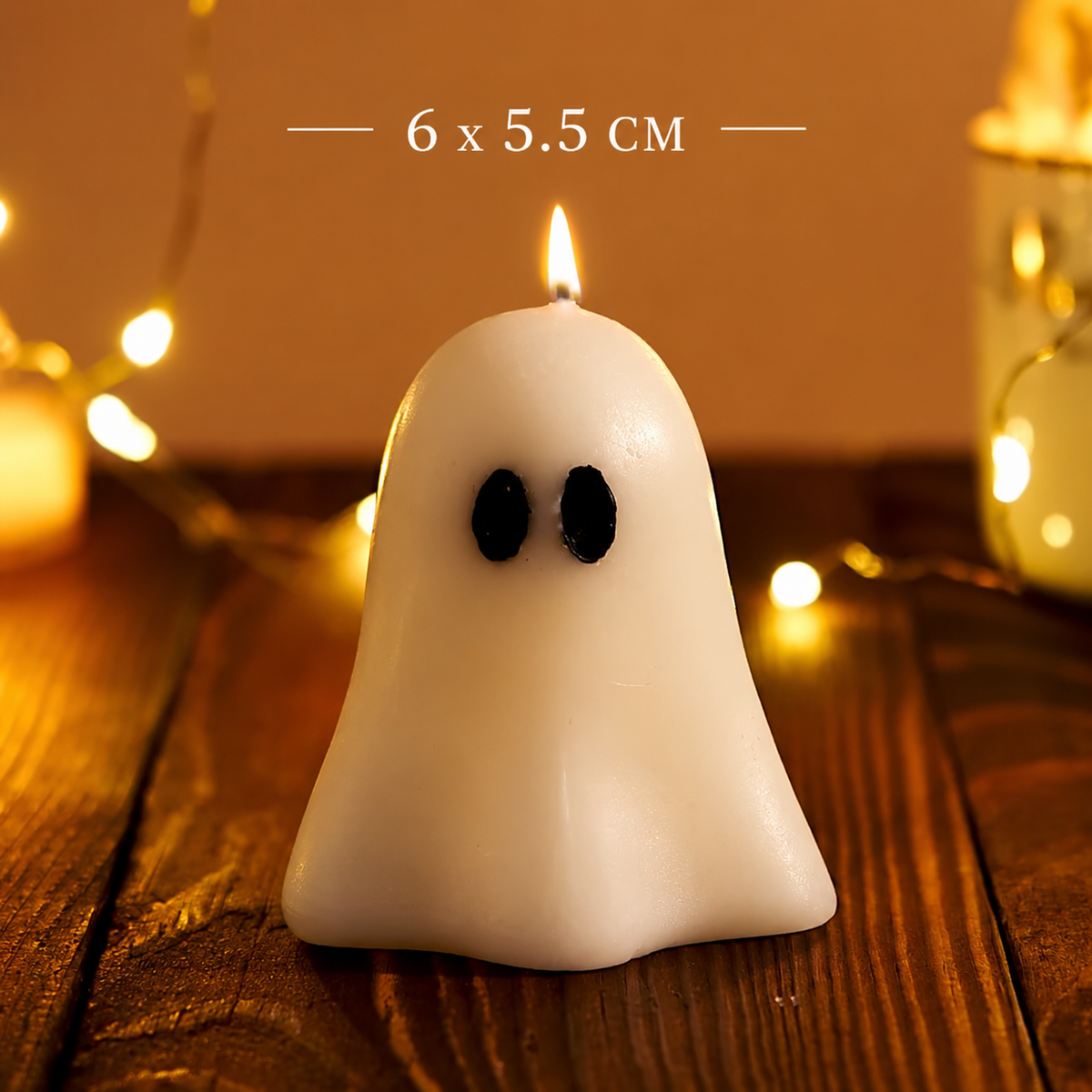 A white ghost-shaped candle with black eyes sits on a wooden surface with warm string lights blurred in the background. White text at the top reads '6 x 5.