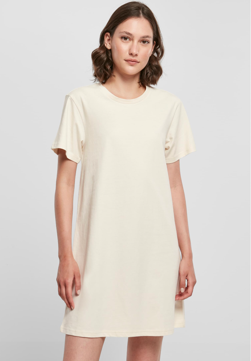 A woman modeling a short-sleeve crewneck t-shirt dress in a solid cream color, photographed against a light gray studio background.