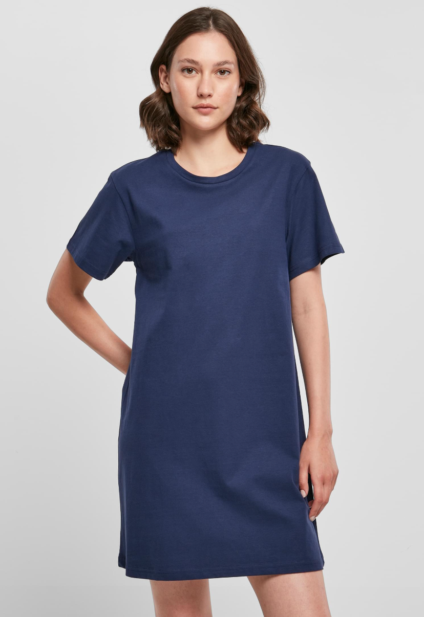 A woman modeling a simple short-sleeve crewneck t-shirt dress in solid navy blue against a light gray studio background.